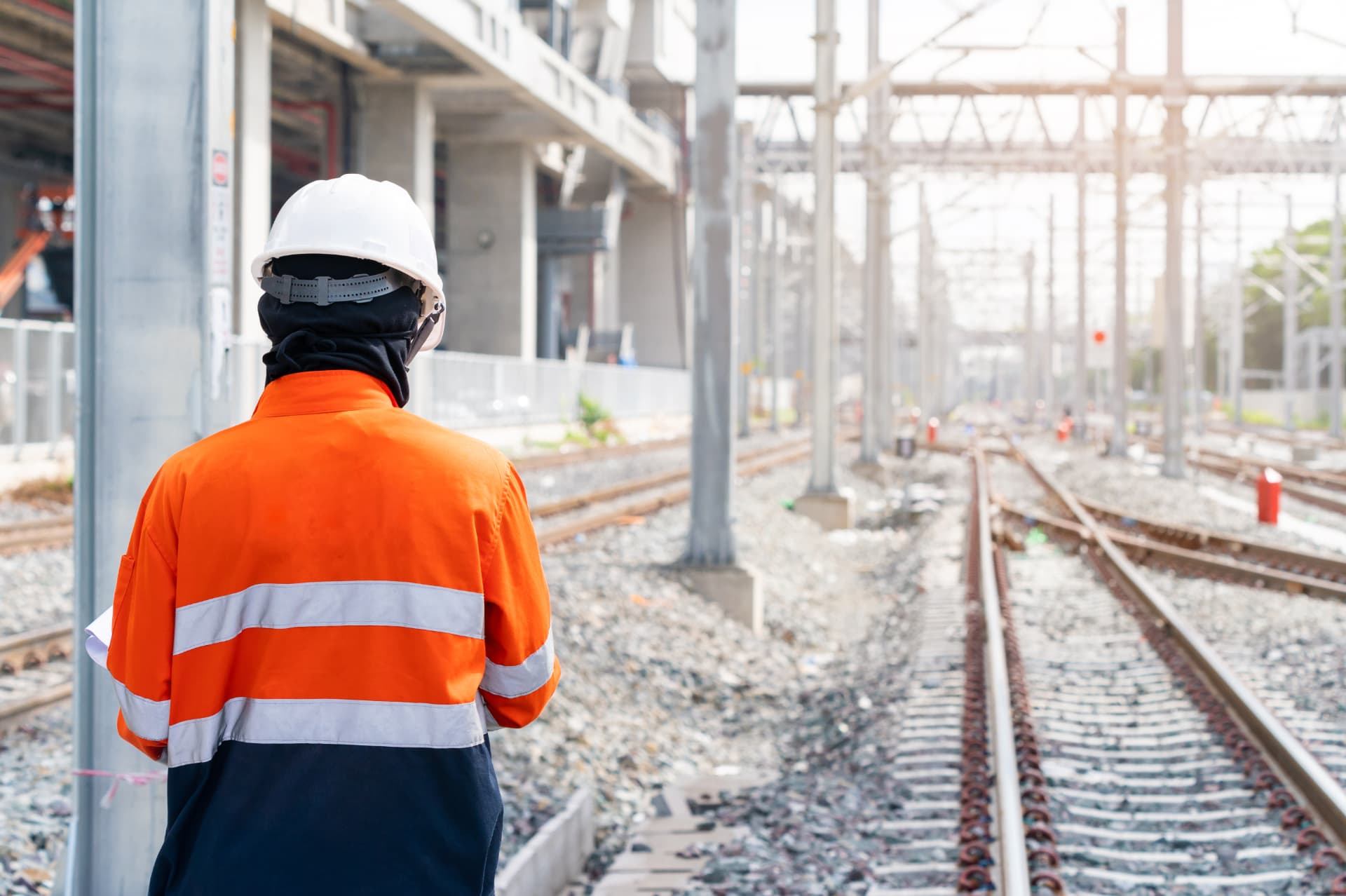 Rail engineer in a white hard hat and orange high-visibility jacket looking along railway tracks
