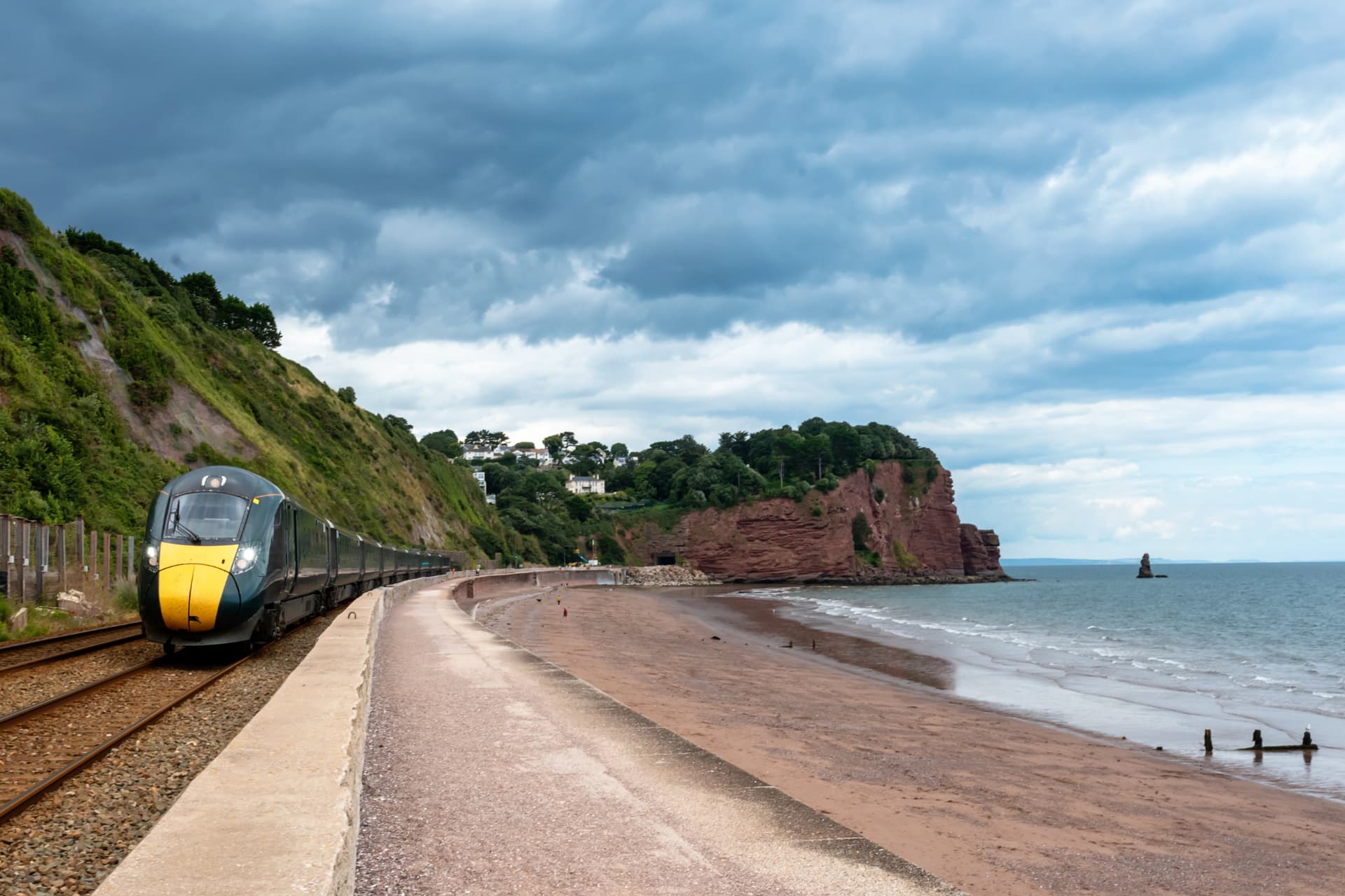 Passenger train running along a coastal sea wall beside a red sandstone beach
