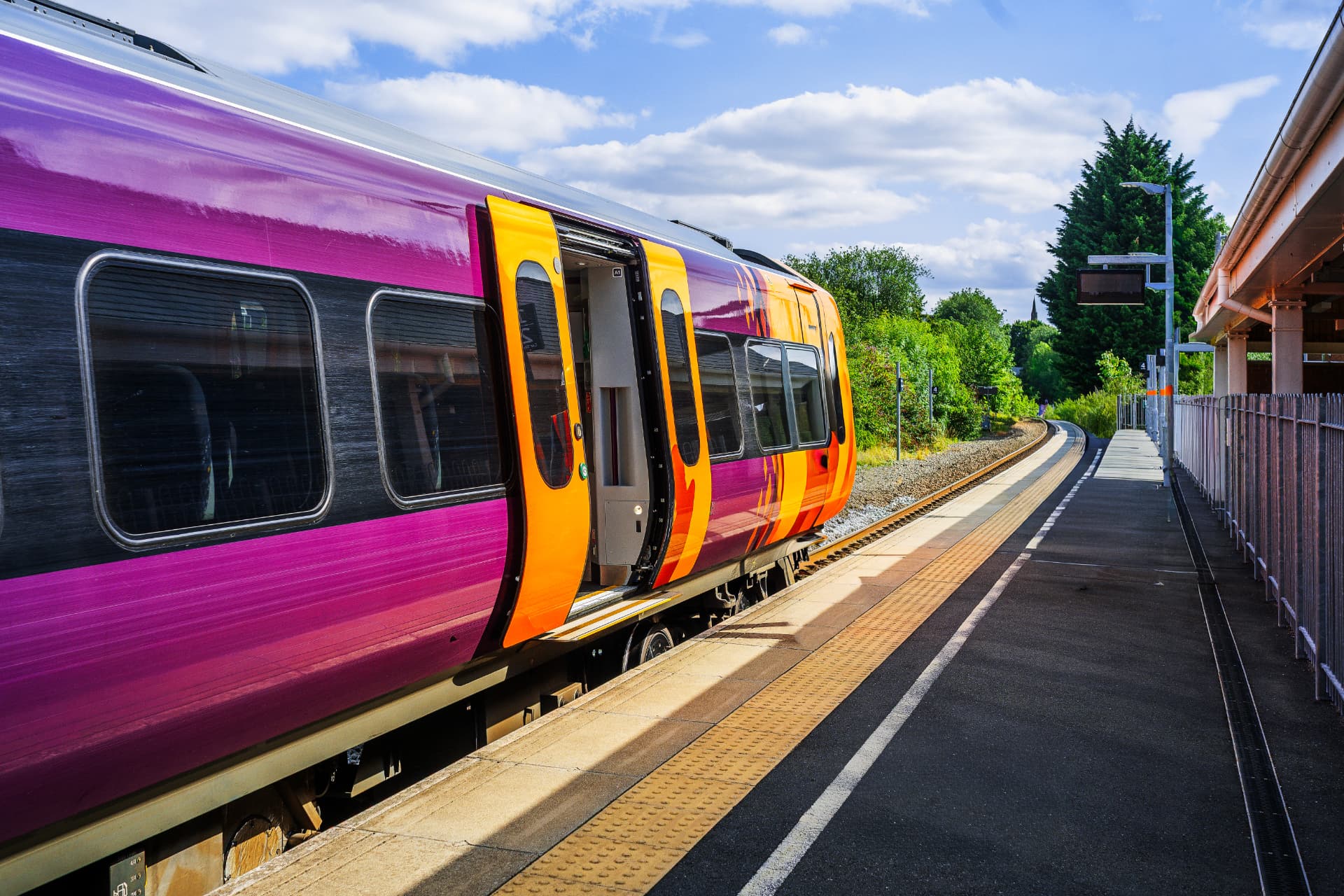 Purple and orange passenger train with doors open at a UK station platform